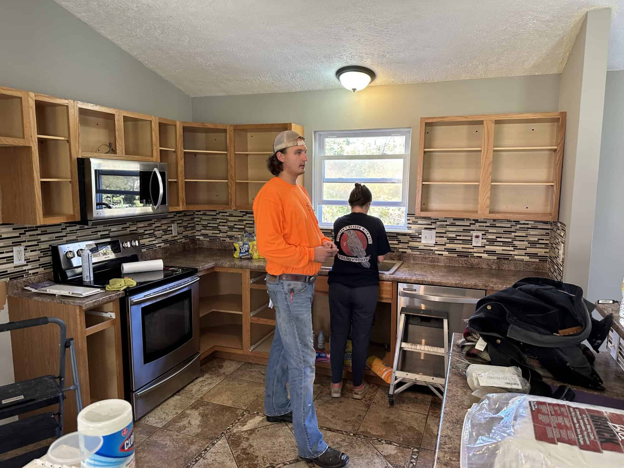 Kitchen renovation in progress by APEX Coating and Painting Services, with workers preparing cabinets and backsplash