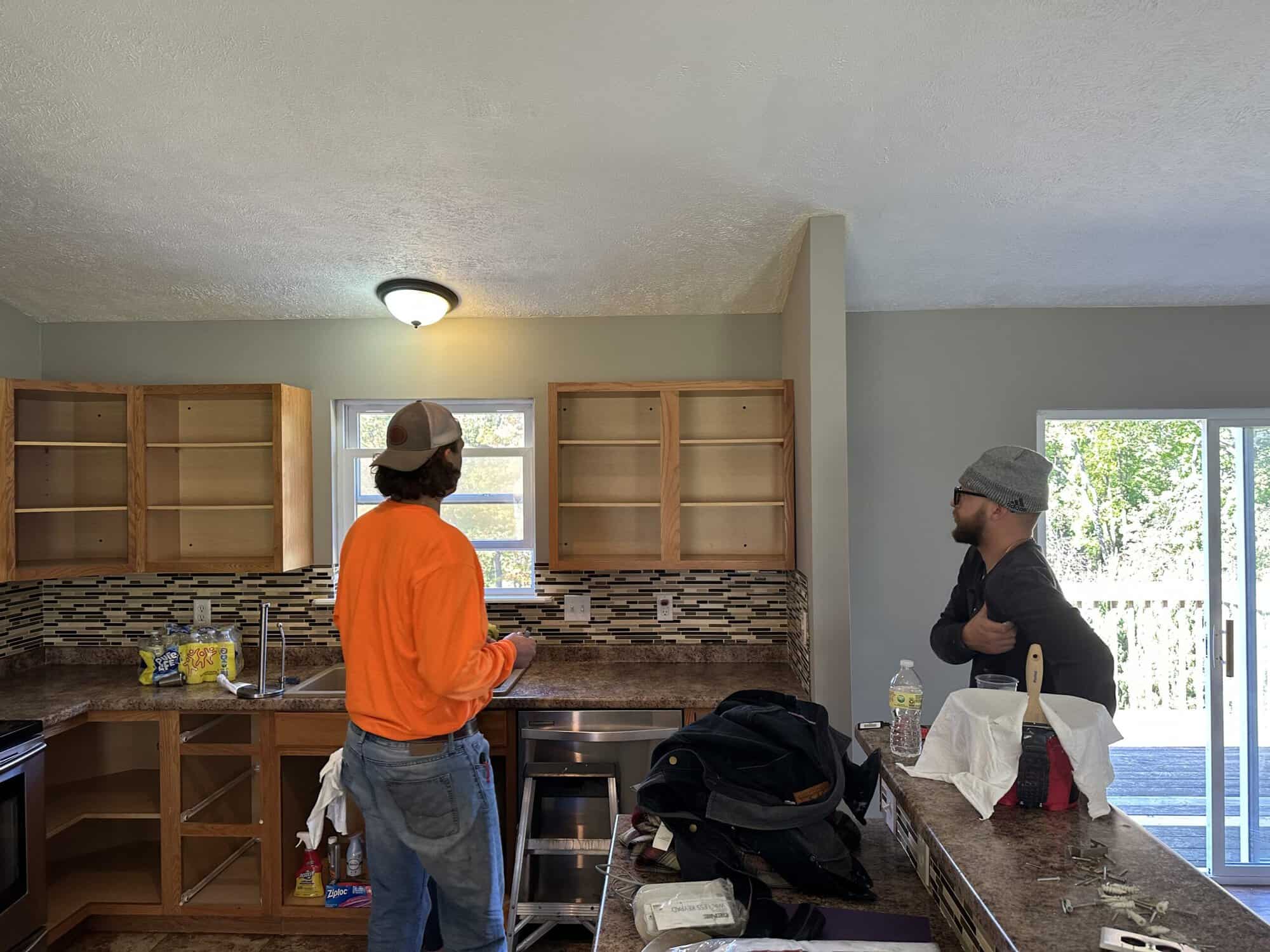 Kitchen renovation in progress by APEX Coating and Painting Services, with workers preparing cabinets and backsplash