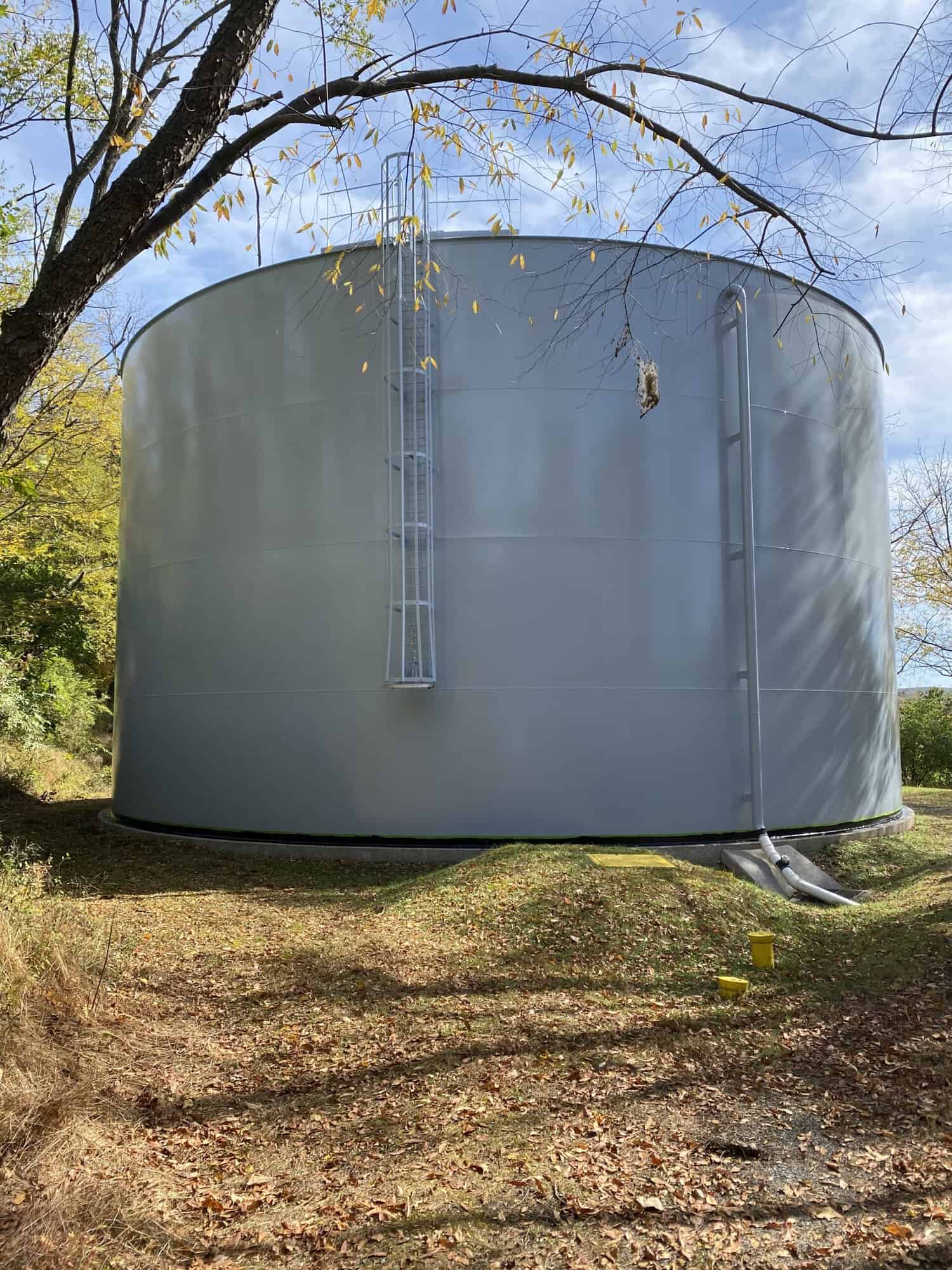 Large industrial water tank painted in light grey by APEX Coating and Painting Services, situated in wooded area