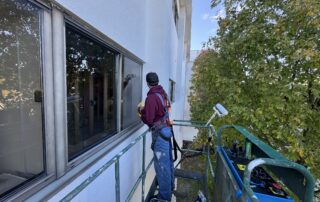 Professional painter with safety harness applying exterior coating to elevated building facade by APEX Coating Services