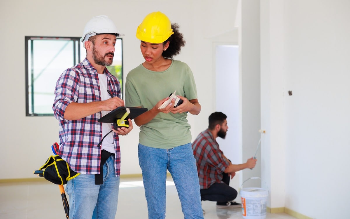 indoors. Painter with roller and color palette. Young african american woman and hispanic construction worker smiling builder people %painting services% - Apex Coating Company, LLC. Why Cabinet Painting Cost Varies So Much Between Contractors (And What You're Really Paying For)